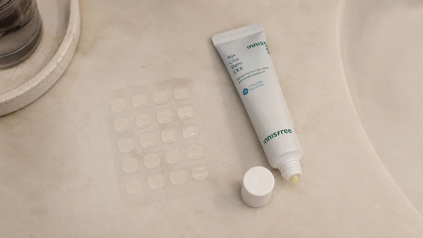 A small round hydrocolloid patch and a tube of spot cream sitting side by side on a bathroom counter