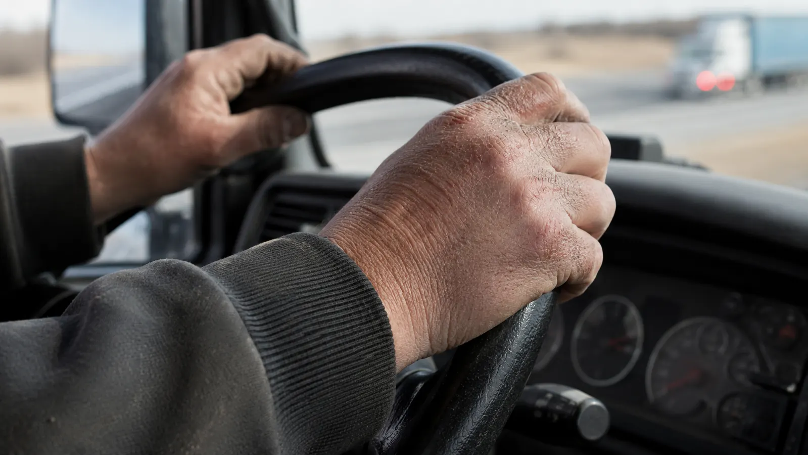 Close-up of rough, work-worn hands with dry knuckles resting on a steering wheel