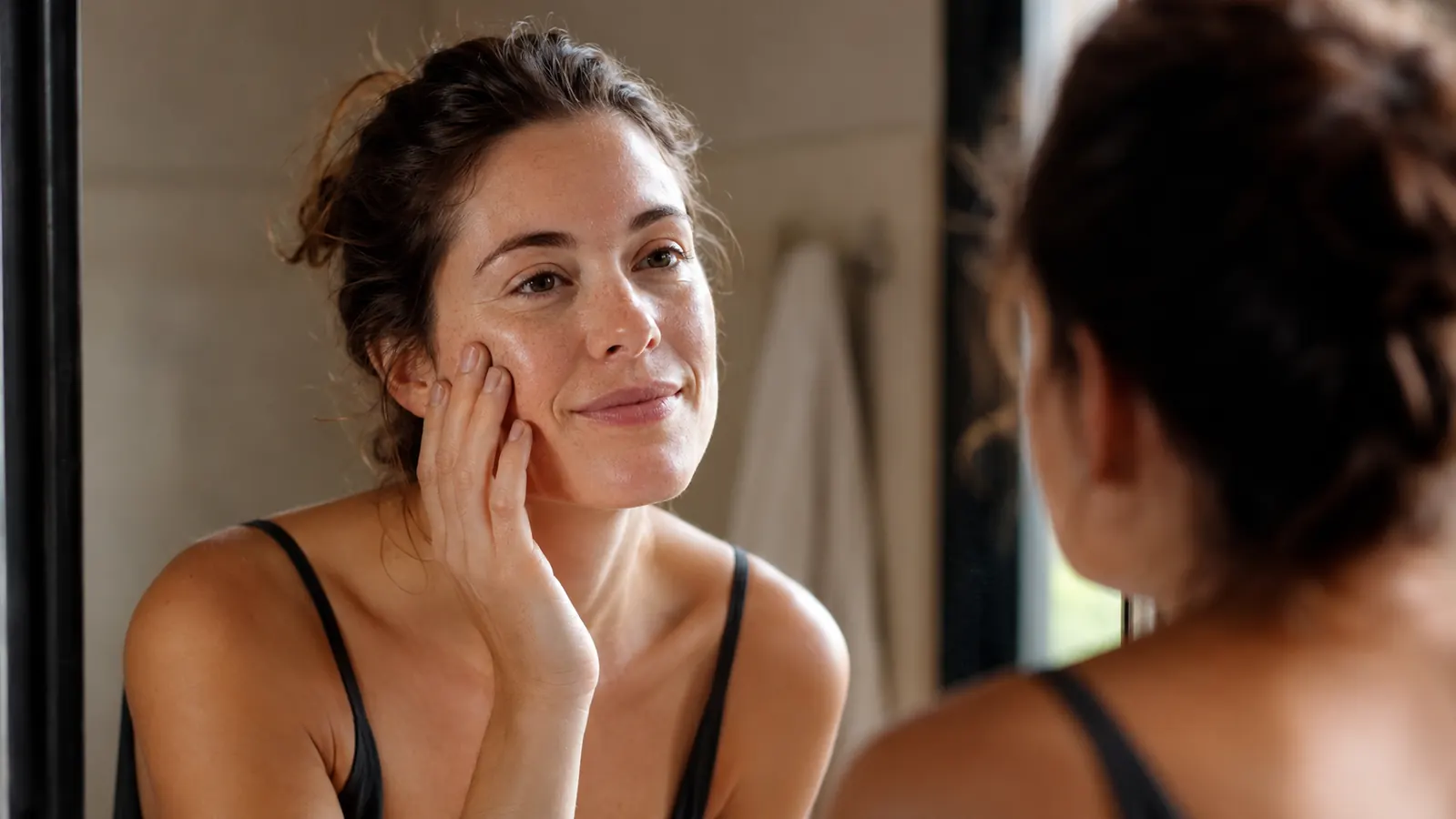 Woman looking at her clear reflection in a bathroom mirror in soft morning light