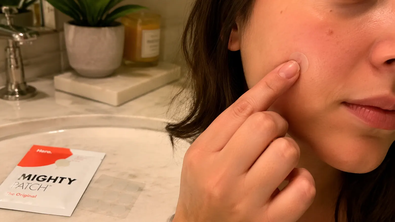 Hand pressing a small round hydrocolloid patch onto a spot on the cheek with a fingertip