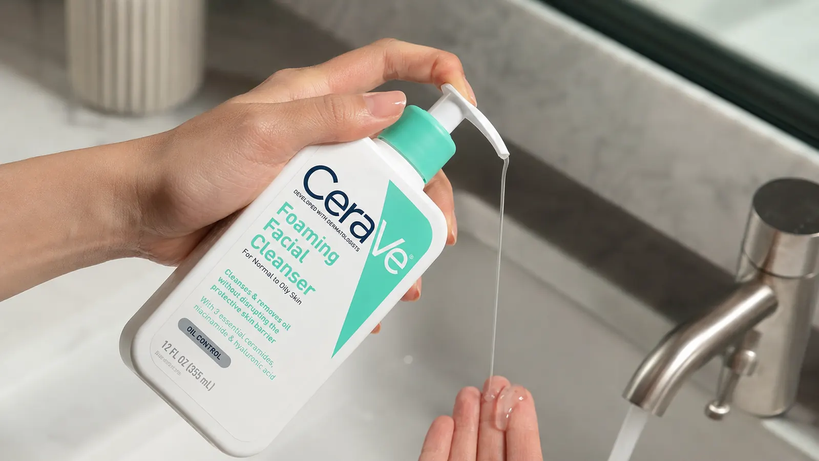 Hand pumping CeraVe Foaming Facial Cleanser onto fingertips over a running faucet