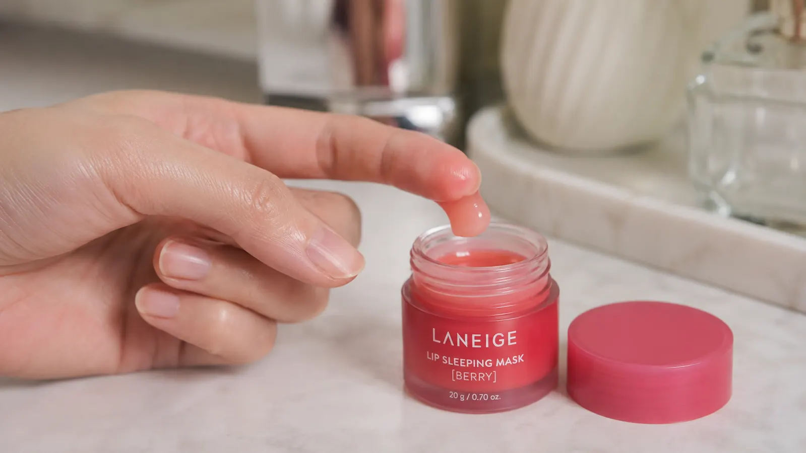Fingertip scooping a small amount of lip sleeping mask from an open jar
