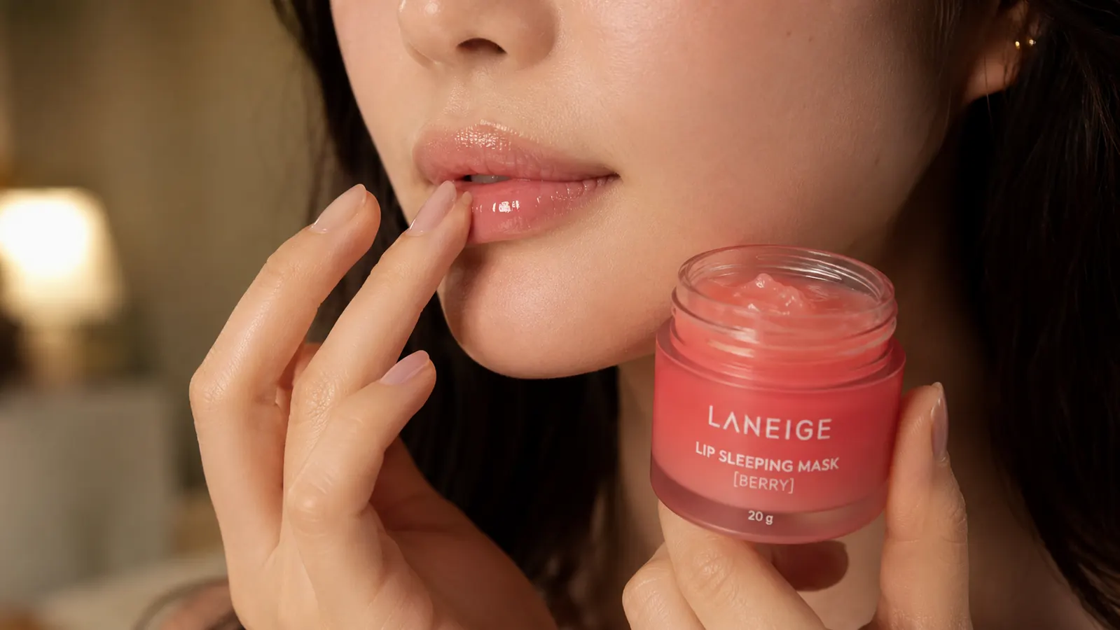 Close-up of a fingertip applying a small amount of pink lip mask balm to the lips