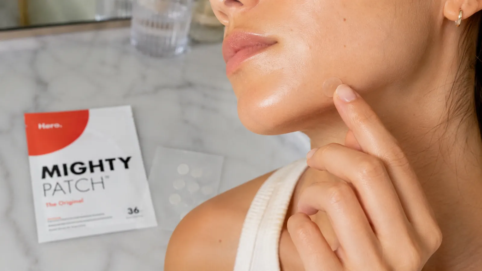 Hand pressing a small round hydrocolloid patch onto a spot near the jawline