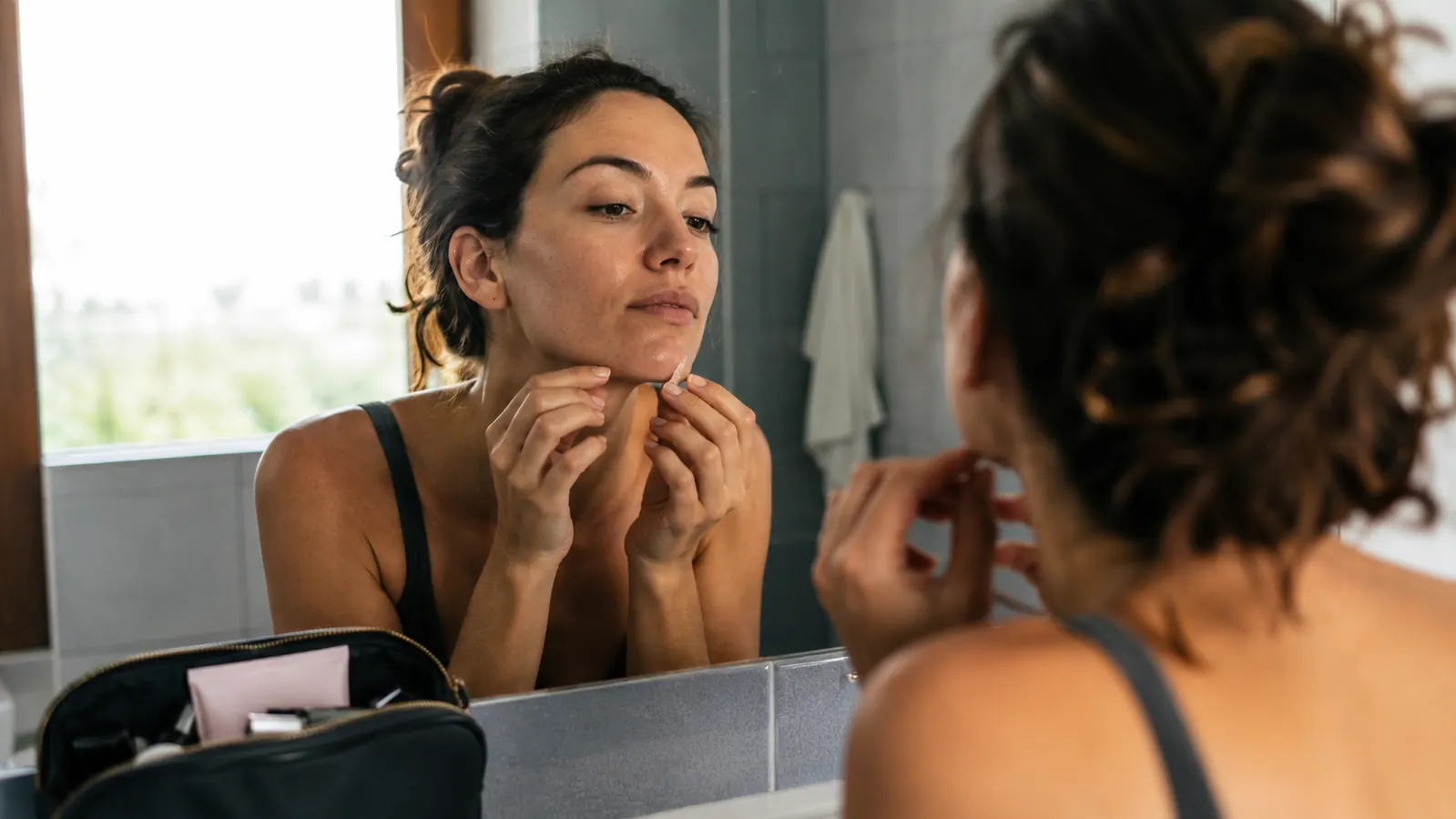 Woman getting ready in the morning, peeling a small patch off her chin before applying makeup