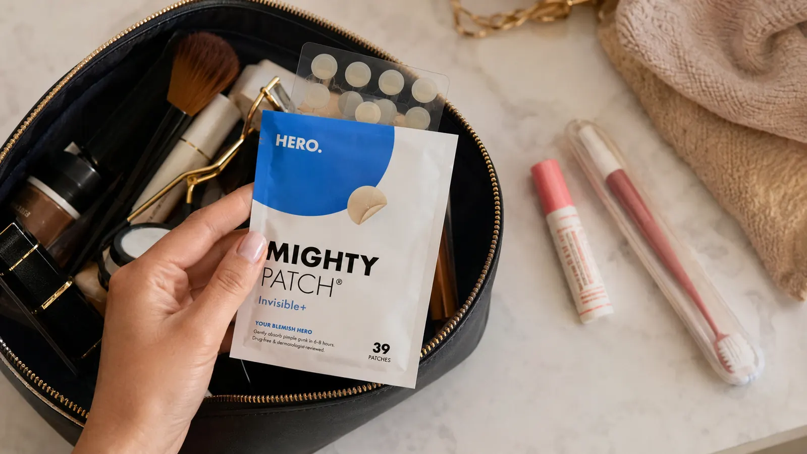 Open makeup bag on a bathroom counter with a strip of hydrocolloid pimple patches tucked inside next to other essentials